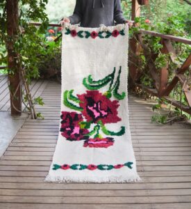 Piecera de cama tejida a telar con un diseño de flores grandes de color rosado y hojas verdes sobre fondo blanco.