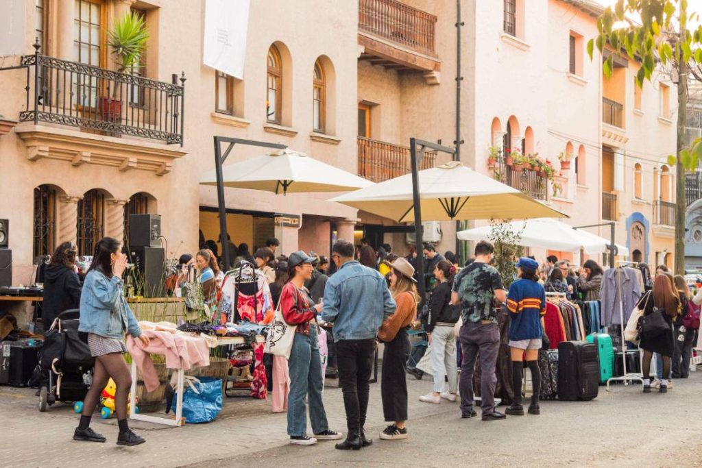 Vista de una calle peatonal concurrida frente a edificios de arquitectura clásica, con quitasoles de terrazas y gente paseando.