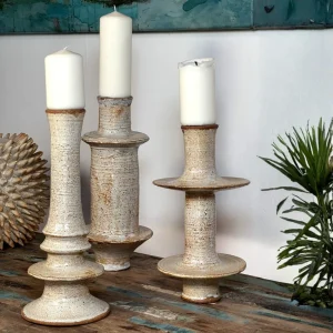 res candelabros rústicos de diferentes alturas sosteniendo velas blancas gruesas